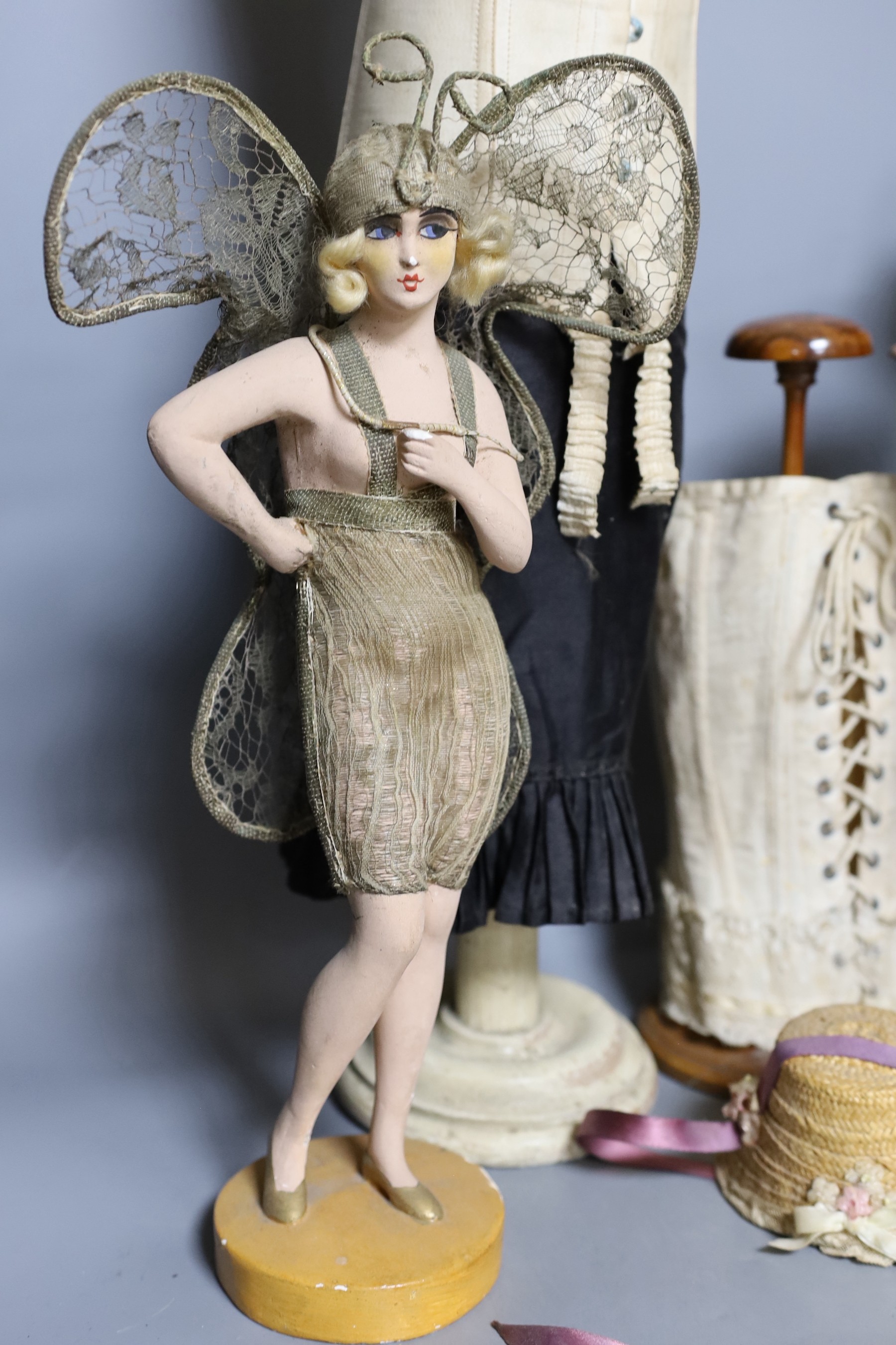 A 1920s/1930s ‘Sanetta’ shop display miniature corset dummy, 59 cm, three miniature corsets, a 1920s painted composition and metal thread decorated butterfly girl figure and other items